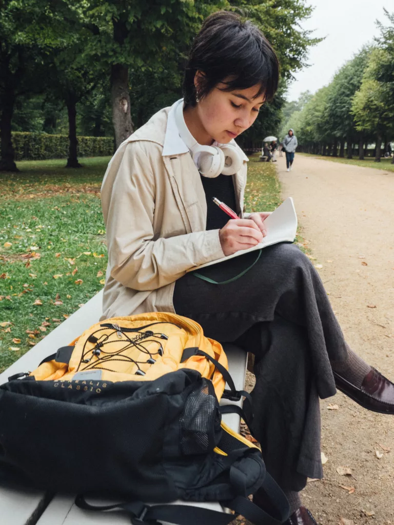 Ung kvinne sitter på en parkbenk og skriver i en bok